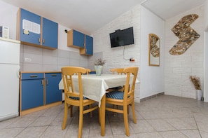 Una cocina compacta con armarios azules, salpicadero de azulejos blancos, un televisor de pantalla plana en la pared y una mesa de comedor con cuatro sillas.
