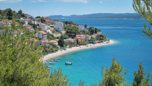 A coastal town with buildings along the beach, boats in the water, and clear blue skies. - Apartments Natalies Dream (Omis)