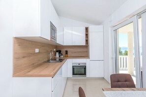 Moderni keittiö, jossa on valkoiset kaapit, puinen työtaso, uuni sekä ruokailutila pöytineen ja tuoleineen.