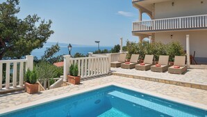 A pool area with lounge chairs and potted plants, overlooking a body of water. - Apartments Natalies Dream (Omis)
