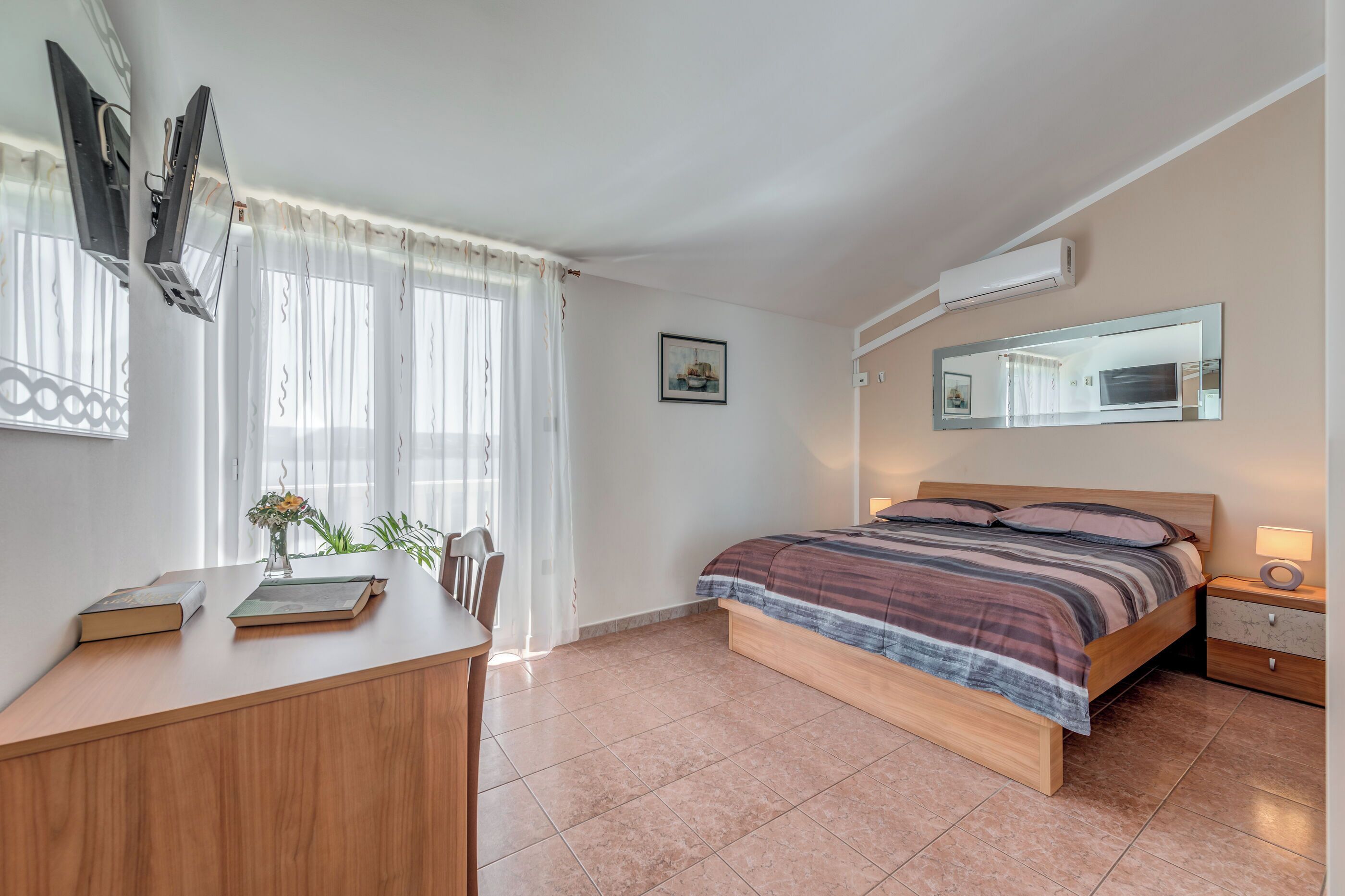A bedroom with a bed, bedside table, and a desk with books and a vase.
