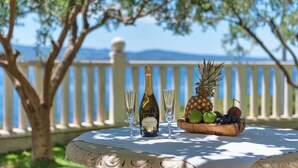 A table with a bottle of DoC Carina wine, two glasses, and a bowl of fruit. - Apartments Natalies Dream (Omis)
