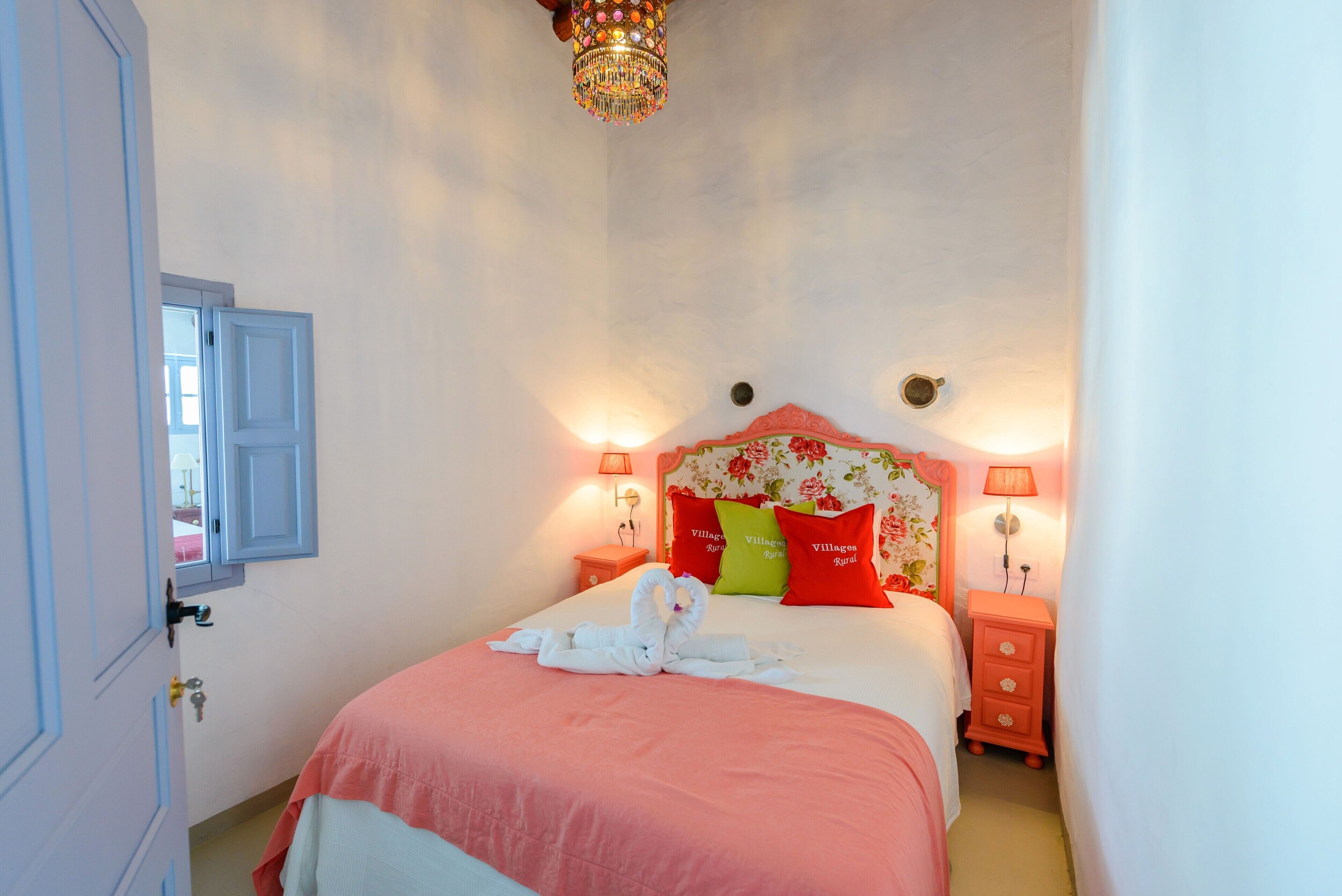 Un dormitorio con una cama, almohadas, una mesita de noche, una lámpara y una puerta.