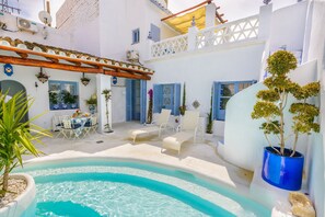 Un patio con piscina, paredes blancas, contraventanas azules y mobiliario exterior.