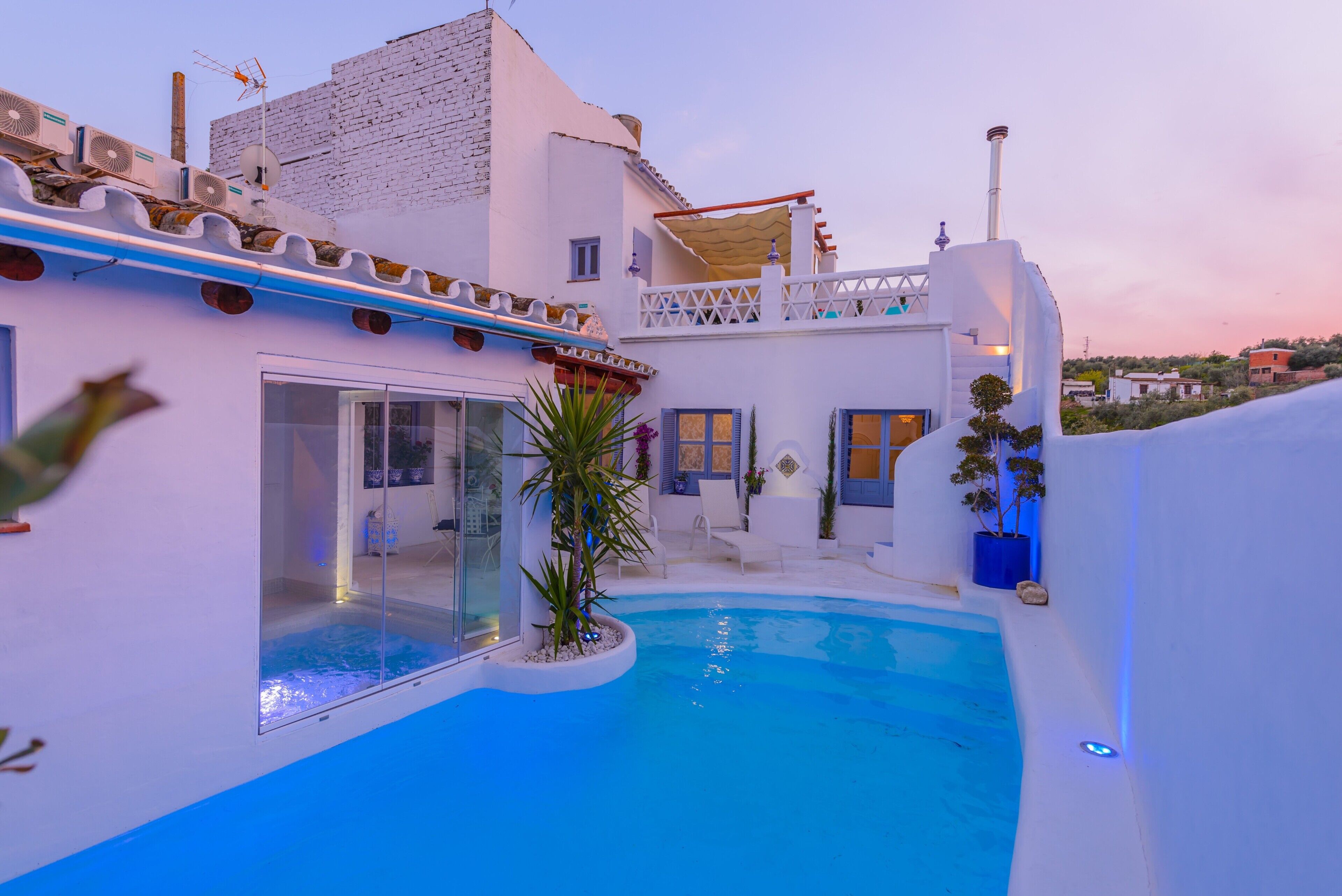 Un edificio moderno con piscina, una sala acristalada y un balcón con mobiliario de exterior.
