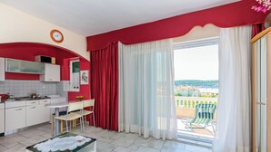 A kitchen with white cabinets, a dining table, and chairs. There is a balcony with a chair and a table. - Apartments Rada i Stanislav (Rab)