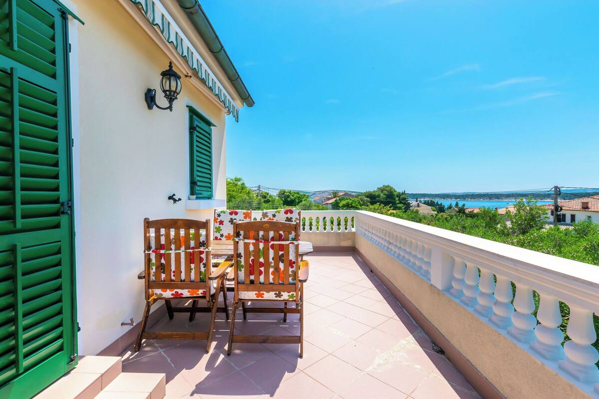 A balcony with two wooden chairs and a table, overlooking a scenic view of a bridge and greenery.