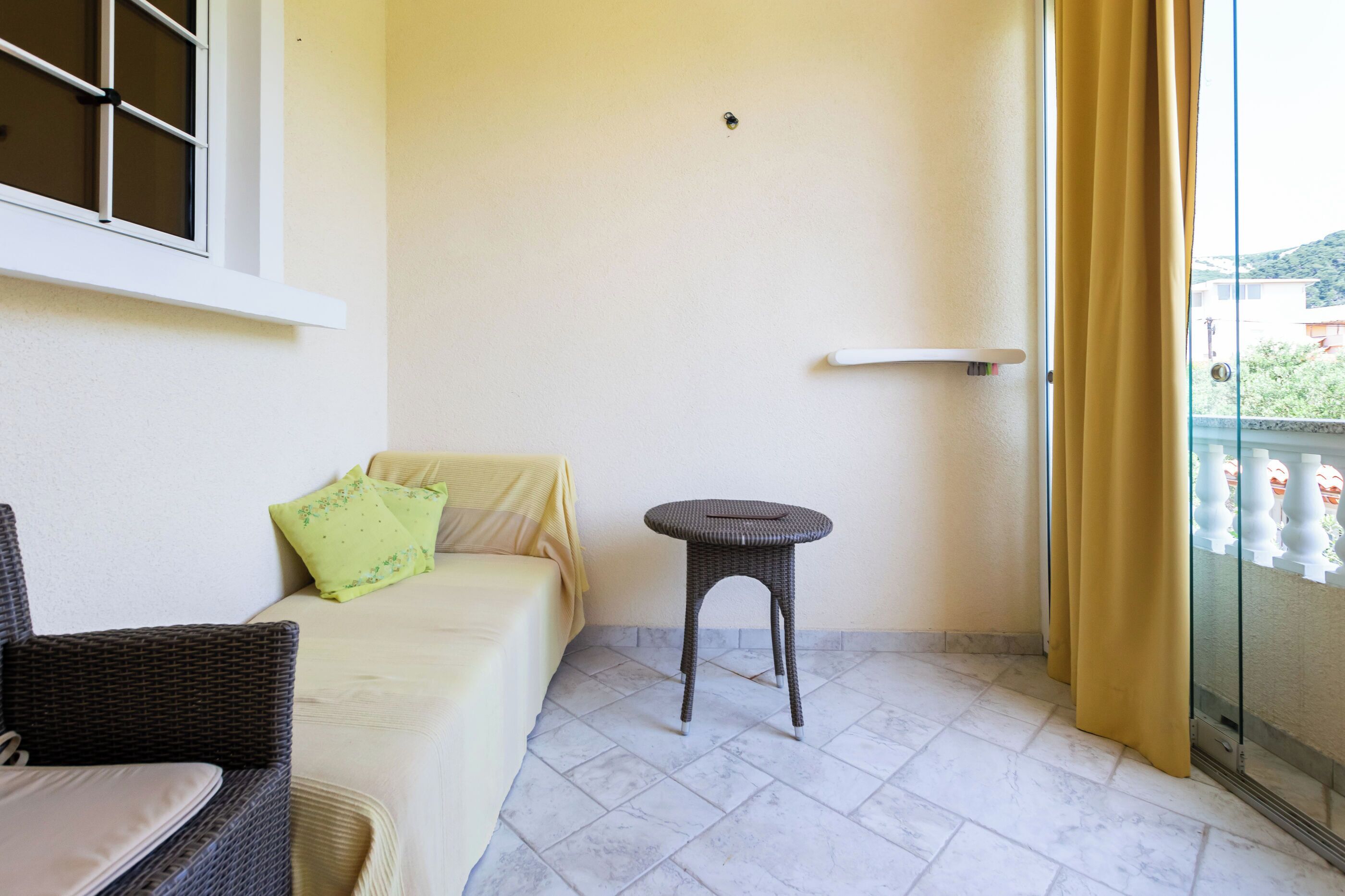 Ein Balkon mit einem Korbstuhl, einem Sofa mit gelber Auflage und einem kleinen Tisch.