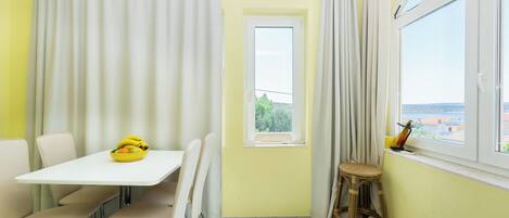 A corner room with a white table, four chairs, a small window, and a view of the outside.