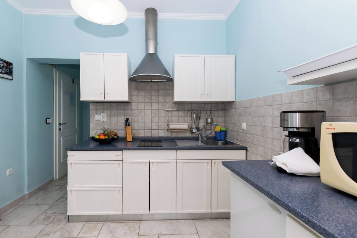 A kitchen with white cabinets, a stainless steel range hood, a sink, and a coffee maker.