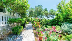 A stone pathway leading through a lush garden with various plants and flowers. - Apartments Rada i Stanislav (Rab)