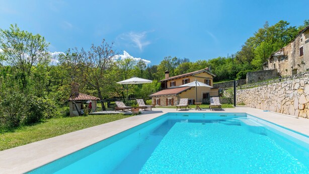 Ein Pool mit Liegestühlen und Sonnenschirmen, umgeben von Grünpflanzen und Steinmauern.