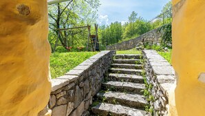 Eine steile Steintreppe führt einen Hügel hinauf, umgeben von Grünpflanzen und einer Steinmauer.