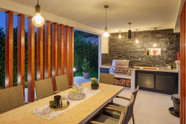 An outdoor dining area with a stone wall, wooden slats, and a grill station. - Villa E&N (Sibenik)