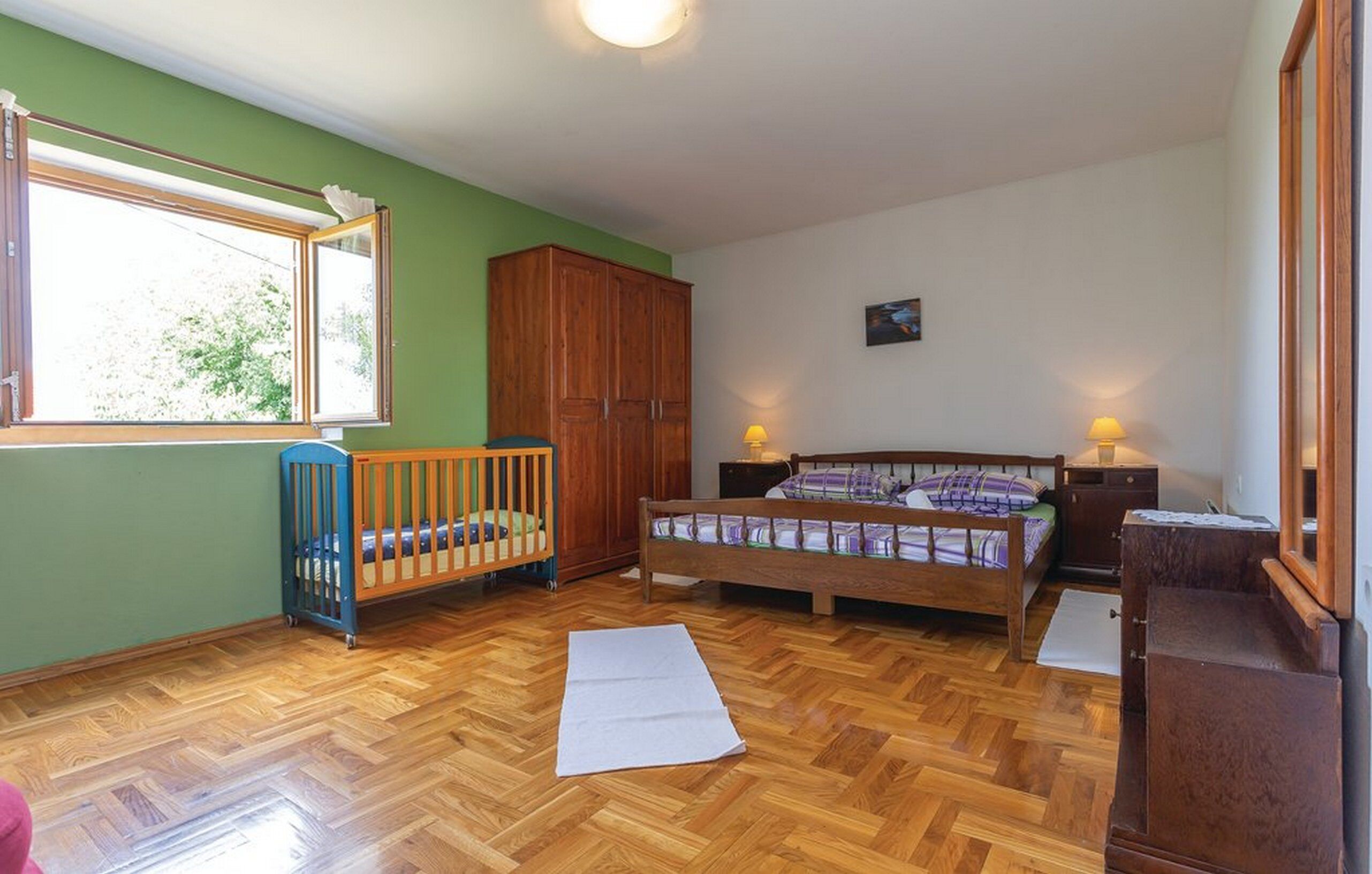 A room with a crib, a bed, a wardrobe, and a window.