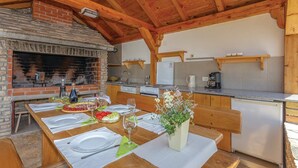A rustic kitchen with a brick fireplace, wooden beams, and a dining area set for a meal. - House Rural Soul (Promina)