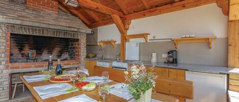 A rustic kitchen with a brick fireplace, wooden beams, and a dining area set for a meal.
