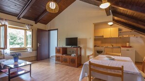 A cozy room with a wooden ceiling, a dining table with chairs, a television, and a kitchen area with cabinets and a dishwasher. - House Rural Soul (Promina)
