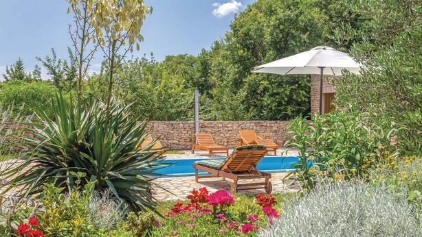 A pool area with lounge chairs and an umbrella, surrounded by lush greenery and flowering plants. - House Rural Soul (Promina)