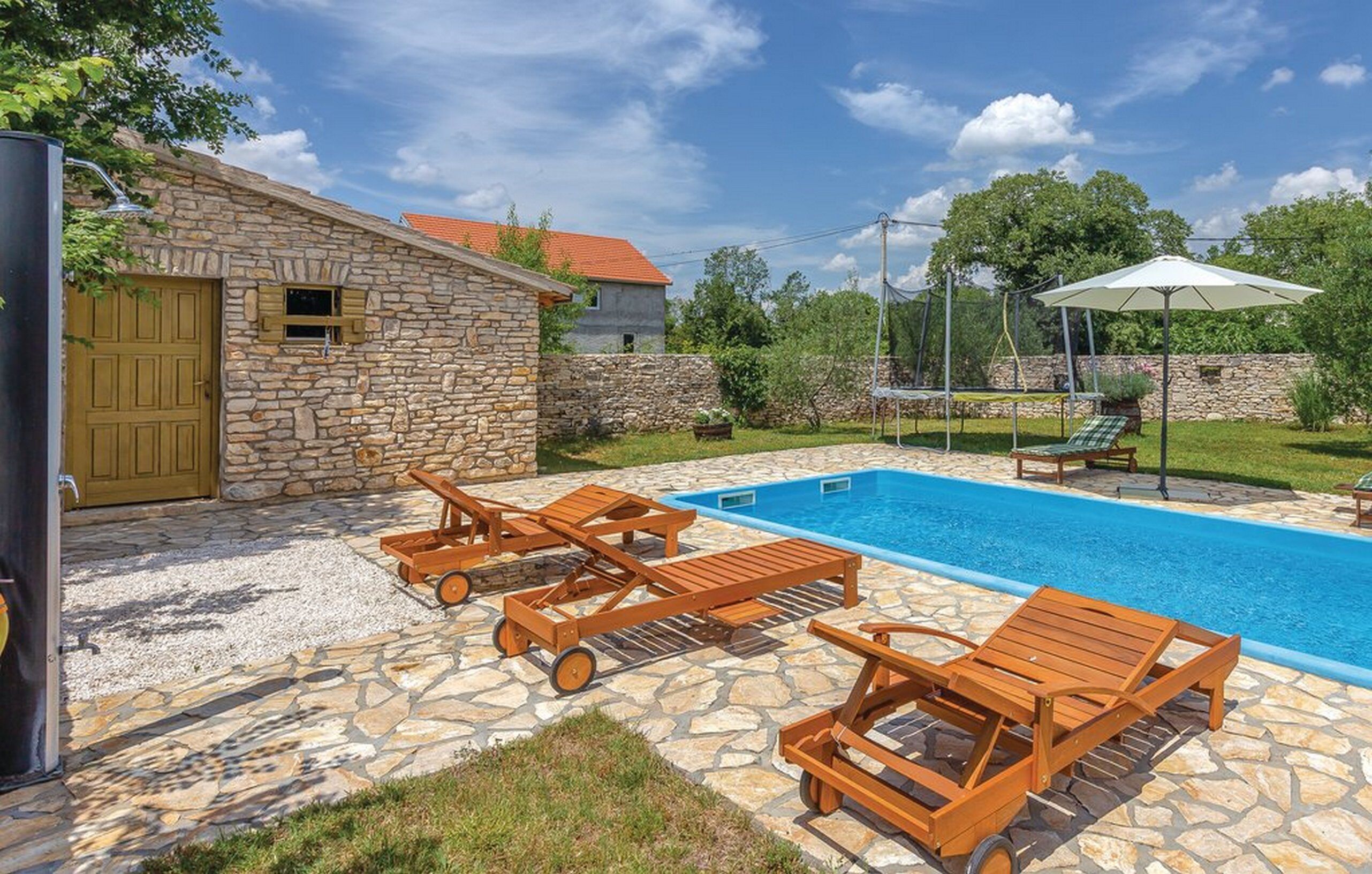 Une maison en pierre avec une piscine, des chaises longues en bois et un jardin.