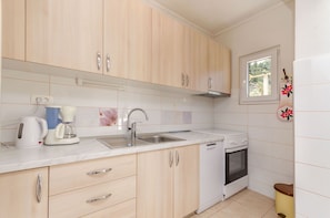 A modern kitchen with light wooden cabinets, a white countertop, a built-in oven, and a window with a view. - Apartment Mare (Trogir)