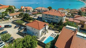 A coastal residential area with a swimming pool, multiple buildings with red-tiled roofs, and a view of the sea. - House Kety (Baska)