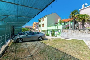 Un coche aparcado bajo una zona con sombra, con un edificio al fondo.
