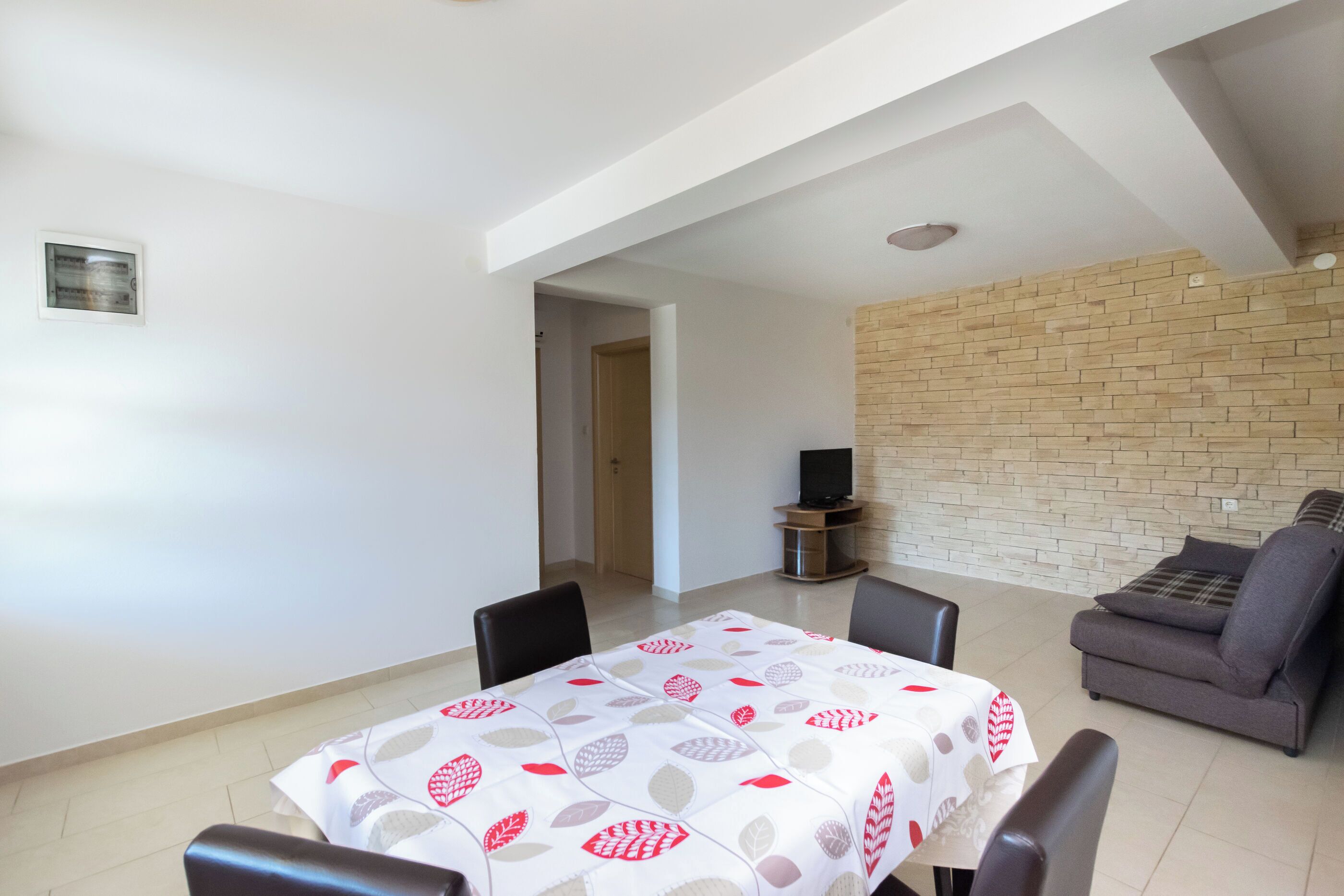 A dining area with a table set for four, a sofa, and a TV stand.