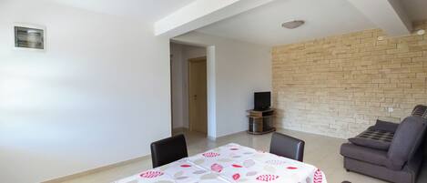 A dining area with a table set for four, a sofa, and a TV stand.