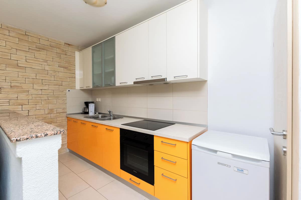 A kitchen with a brick wall, white cabinets, an orange countertop, a black oven, and a white refrigerator.