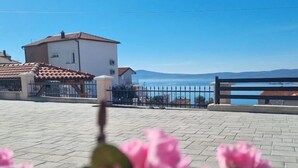 A paved outdoor area with a building in the background, a metal fence, and a clear sky. - Apartments Valentina (Crikvenica)