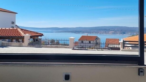 A view from inside a building with a window overlooking a coastal area with houses and a body of water. - Apartments Valentina (Crikvenica)