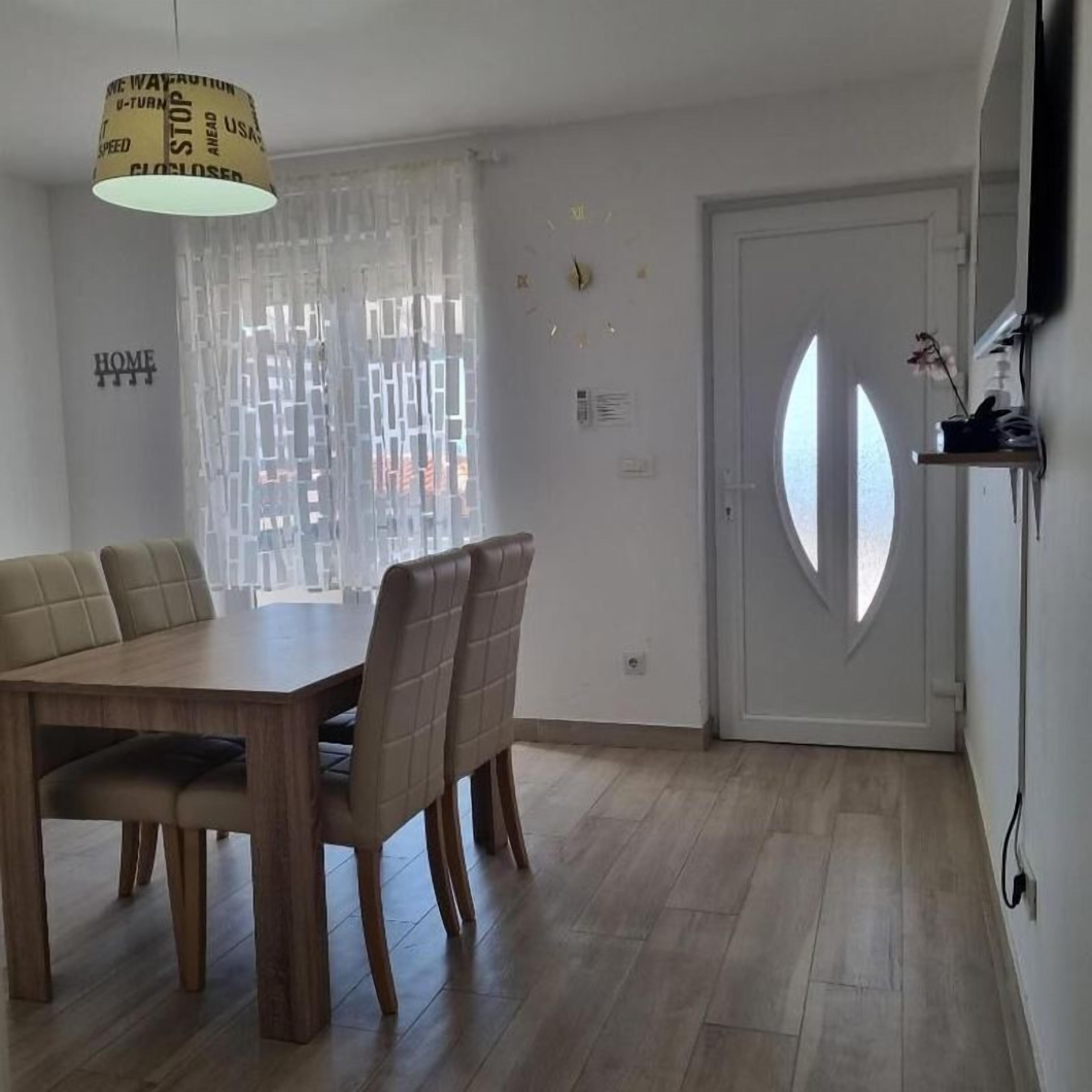 Ein Essbereich mit Holztisch und Stühlen, einer Hängelampe, einem Fenster mit Aussicht und einer Tür mit markantem Design.