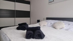 A neatly made bed with rolled towels, a white patterned bedspread, and a painting of a beach scene on the wall. - Apartments Valentina (Crikvenica)
