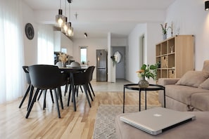 Ett modernt vardagsrum med en soffa, en matplats med stolar, en bärbar dator på ett sidobord och ett kök i bakgrunden.