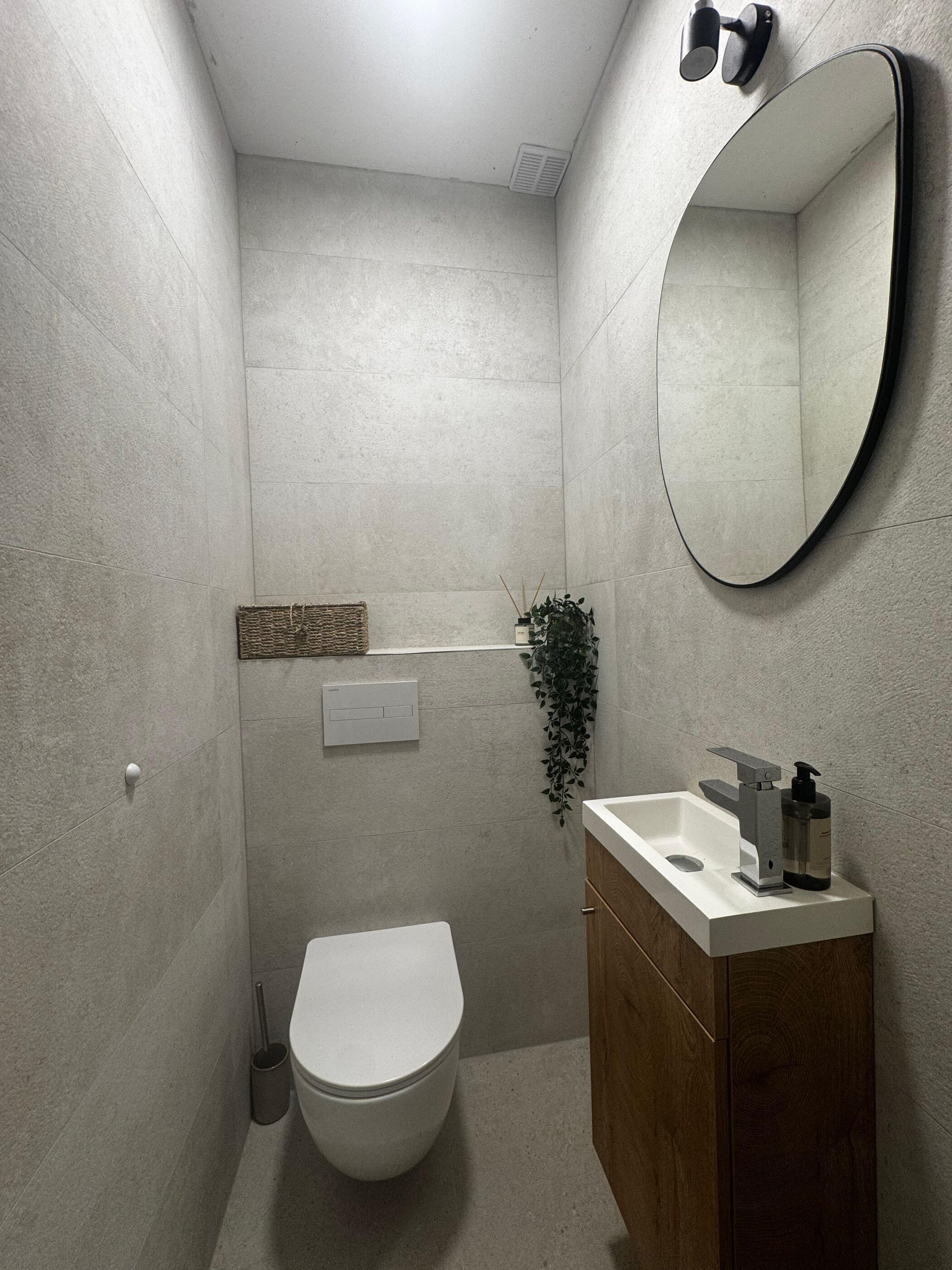 A bathroom with a toilet, sink, mirror, and a wall-mounted light fixture.