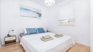 A neatly arranged bedroom with a bed, pillows, a nightstand, a lamp, and a painting on the wall. - Apartments Tonka (Primosten)