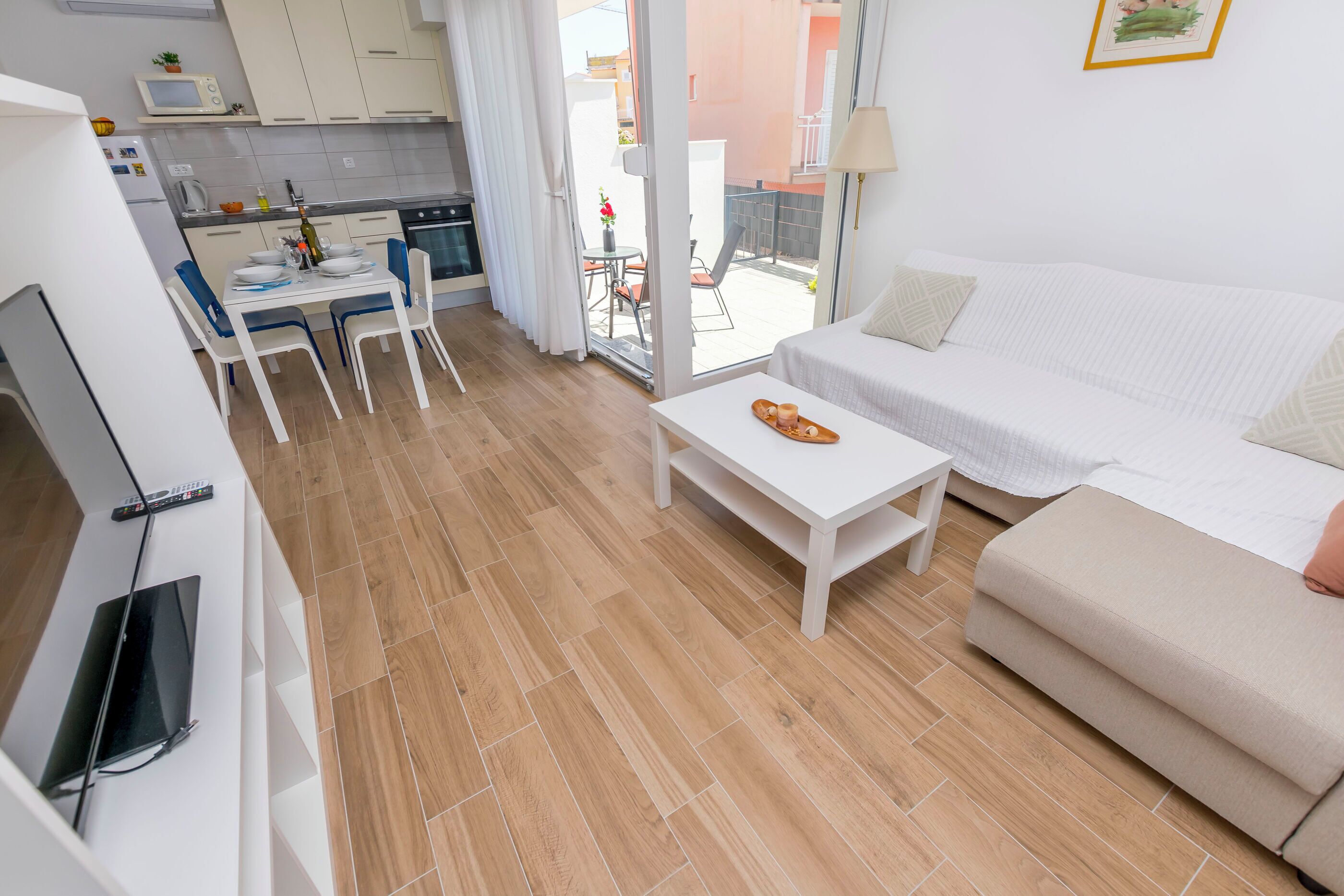 Una habitación de hotel moderna con kitchenette, zona de comedor y sala de estar con sofá y pequeña mesa.