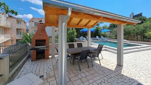 An outdoor patio with a brick oven, a pool, and lounge chairs. - Apartments Mile (Split)