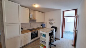A compact kitchen with white cabinetry, a built-in oven, and a small dining area with a chair. - Apartments Mile (Split)