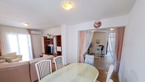 A living room with a sofa, a TV, and a dining table with chairs. - Apartments Mile (Split)