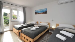 A hotel room with two beds, a window with curtains, a painting on the wall, and an air conditioning unit. - Apartments Plomin (Krsan)