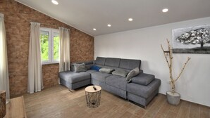 A modern living room with a grey sectional sofa, a round coffee table, and a stone accent wall. - Apartments Plomin (Krsan)