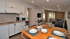 A modern kitchen with white cabinets, a wooden dining table set with plates and glasses, and a grey mat. - Apartments Plomin (Krsan)