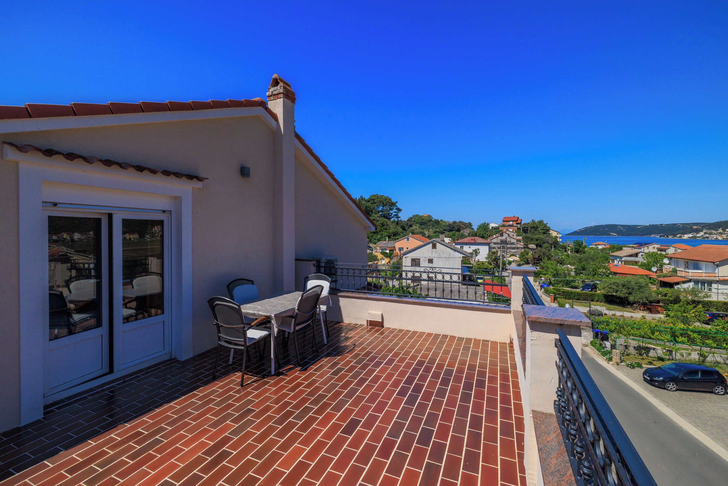 A balcony with a table and chairs, a view of the sea, and a town in the background.