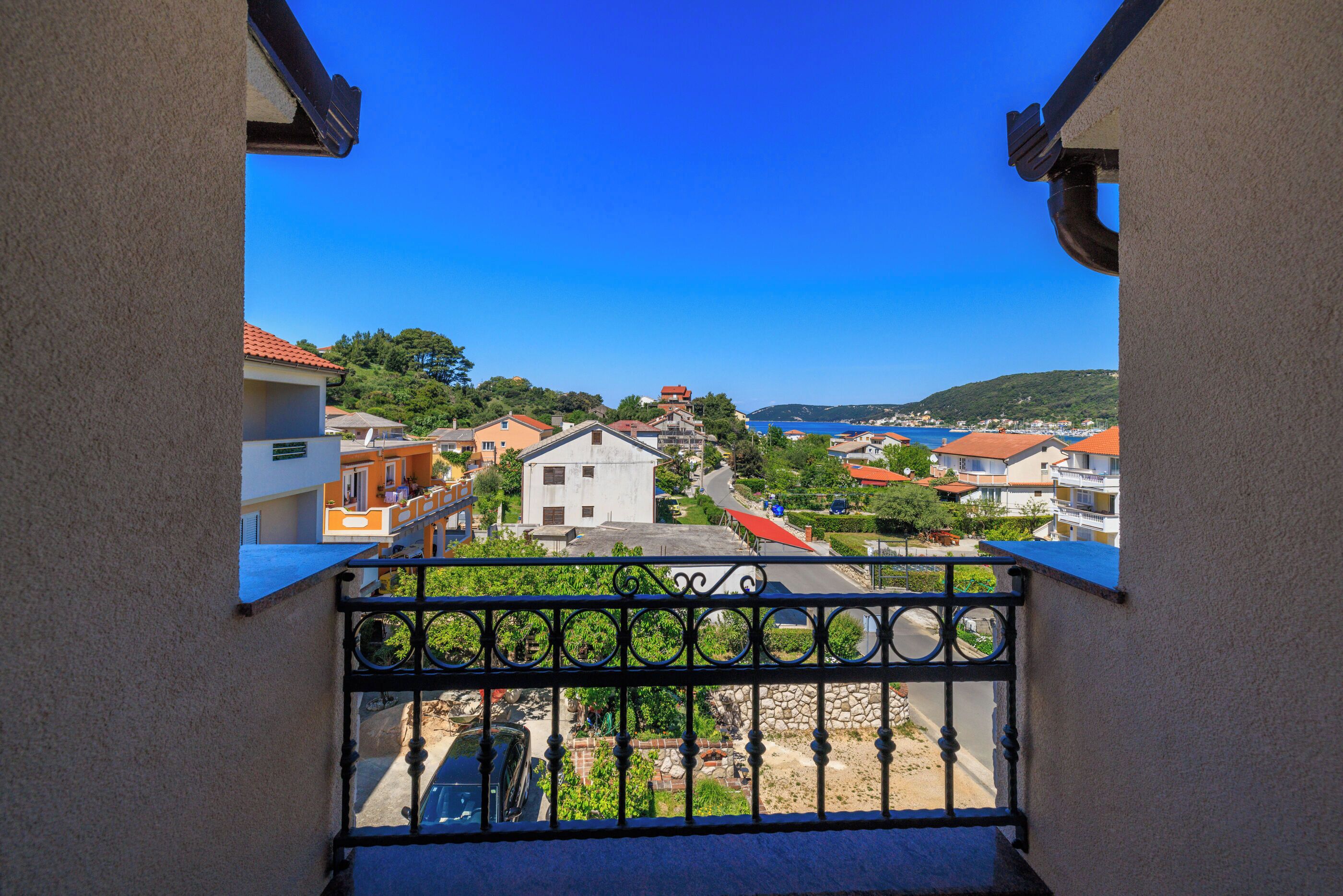 A balcony with a view of a coastal town, including buildings and a clear blue sky.