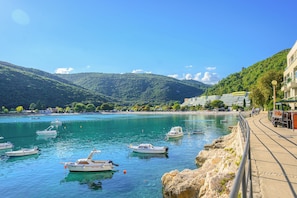 Paesaggio costiero con imbarcazioni ormeggiate lungo la riva, una spiaggia e montagne sullo sfondo.