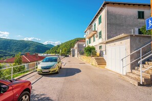 Una stretta via con un'auto parcheggiata a sinistra e un edificio con una insegna blu a destra.