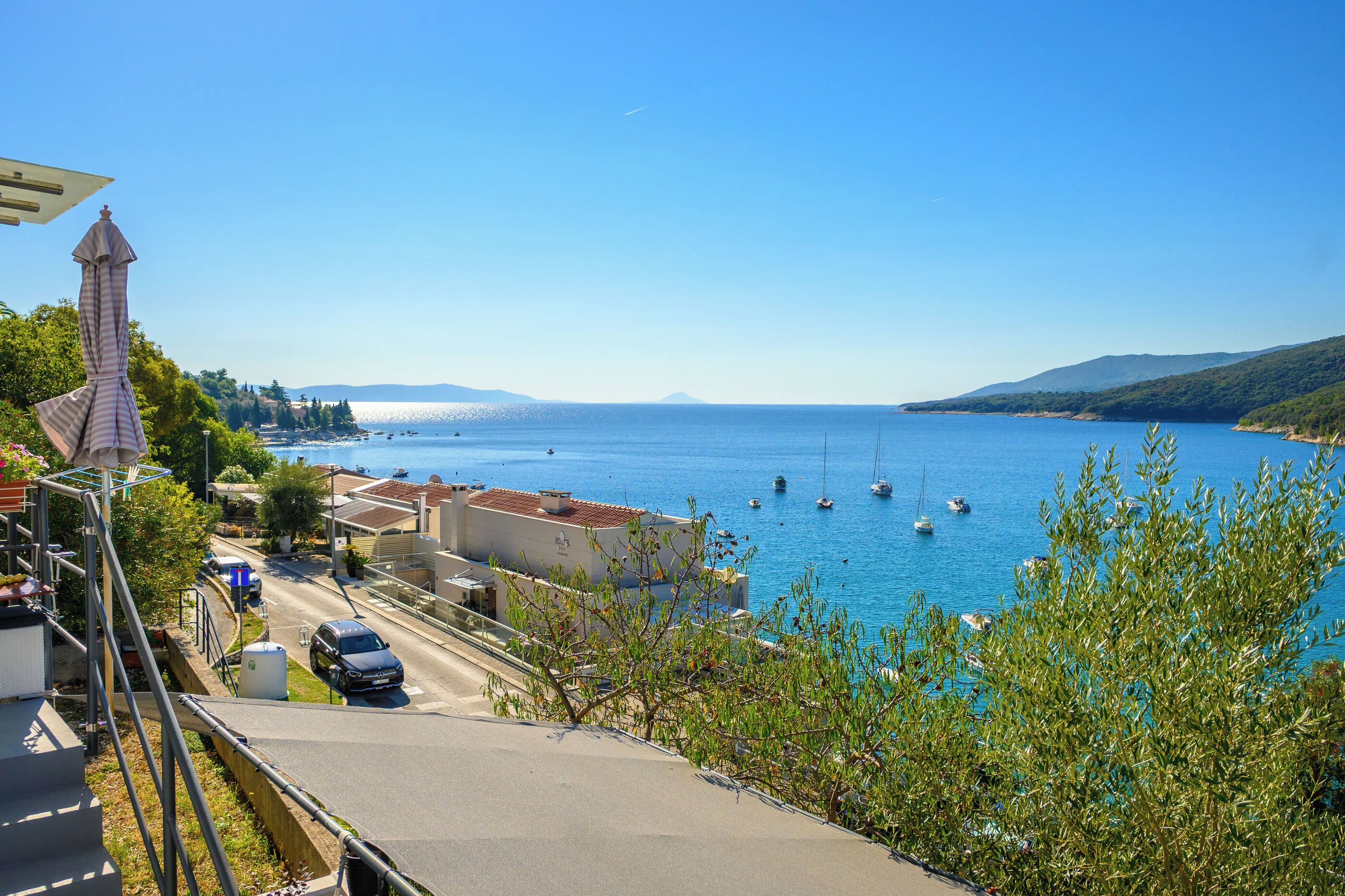 A coastal town with a clear view of the sea, boats, and a road with parked cars.