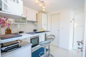 A compact kitchen with white cabinets, a built-in oven, a microwave, and a small dining area with a bar stool. - Apartment By the Sea (Labin)